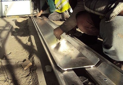 This image depicts workers installing a floor expansion joint cover on a construction site.