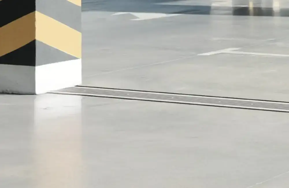 A black and yellow striped safety pillar stands next to an expansion joint on a smooth concrete floor in a parking garage.